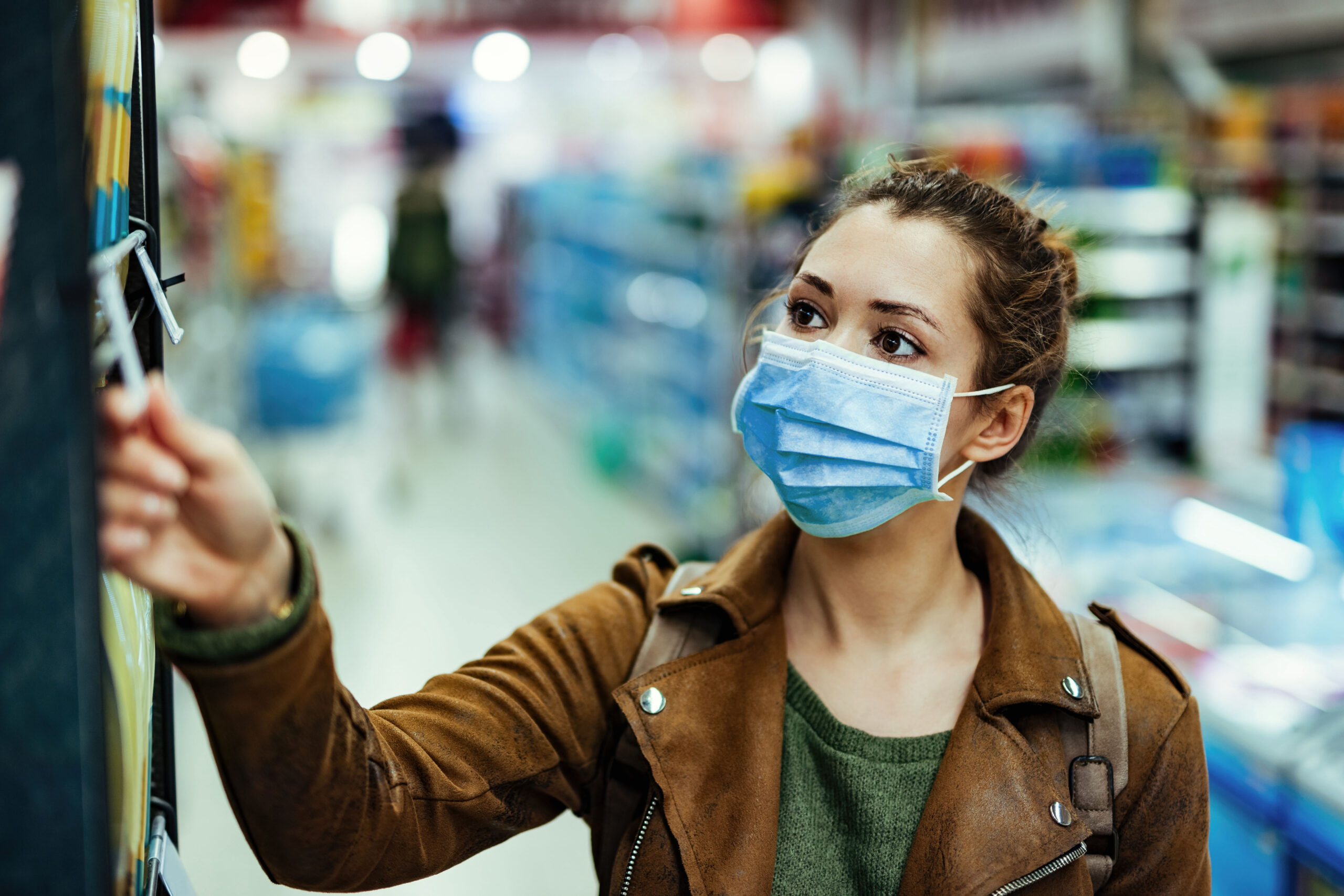 Young woman with protective mask on her face buying in supermarket during coronavirus pandemic.